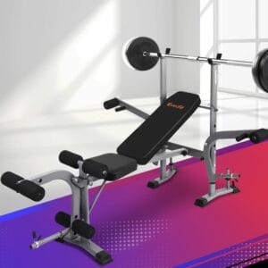 Everfit multi-functional weight bench in bright room with large windows, incline position, barbell and weight plates on rack, leg extension and curl attachments, and gradient flooring with purple-red hues