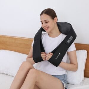 person sitting on bed using black Shiatsu neck and shoulder massager with control panel showing ON/OFF, MODE, and HEAT buttons, holding arm loops to adjust pressure while relaxing in bedroom setting