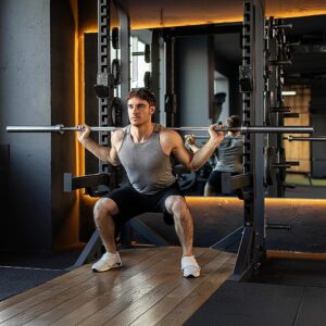 Lifestyle image of a person performing a squat with a 7ft 20kg Olympic barbell in a gym squat rack, wearing a grey sleeveless shirt and black shorts