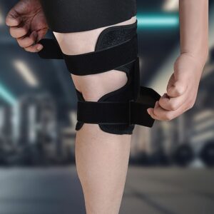 Close-up of leg with black knee brace; person adjusting lower strap in gym setting for secure fit