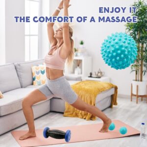 A person performing a lunge stretch on a yoga mat in a bright living room while using massage tools for recovery. A black textured massage roller with blue ends sits near the front foot, while two small blue spiky massage balls are positioned under the back foot. A large floating image of a blue spiky massage ball appears on the right. The background includes a sofa with cushions, a yellow blanket, indoor plants, and a water bottle. Text at the top reads “ENJOY IT THE COMFORT OF A MASSAGE,” highlighting relaxation and post-workout muscle relief.