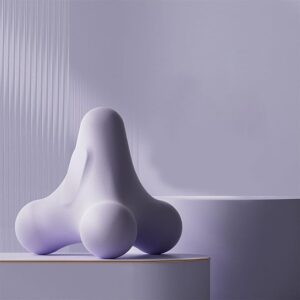 Minimalist studio image of a three-pronged handheld massage tool in a soft matte purple finish, placed on a round pedestal against a light neutral background with subtle vertical texture. The tool features three rounded nodes designed for targeted trigger point therapy and deep tissue relief. The smooth ergonomic shape allows for controlled pressure application on muscles, with soft lighting highlighting the contours and clean design.