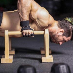 Athlete performing push up exercises on parallettes while wearing weight lifting gloves with wrist support and enhanced grip protection