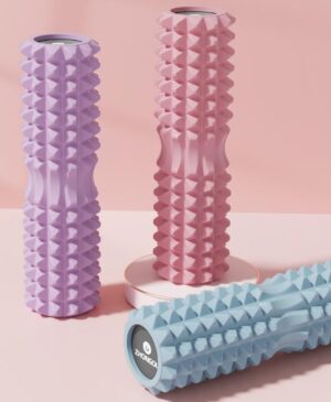 Three textured foam massage rollers displayed in pastel colours including pink, purple, and blue, arranged upright and laid horizontally on a soft pink background. Each roller features a raised geometric surface designed for deep tissue massage and muscle relief, with a hollow core visible at the ends and a branded cap labeled “ZHONGOU.”