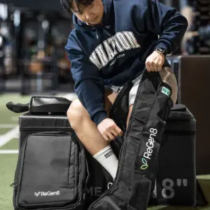 Person fitting a ReGen8 Nyx compression boot beside carry bag