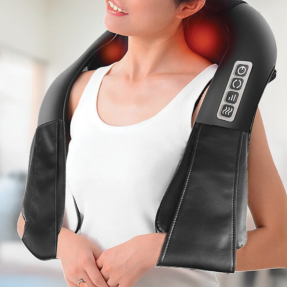 Black heated neck and shoulder massager worn over a white top, showing red heat lights and side controls.