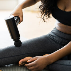 Person using the Remology massage gun on their upper leg while seated on a mat
