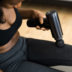 Person using the Remology massage gun on their thigh in workout clothes