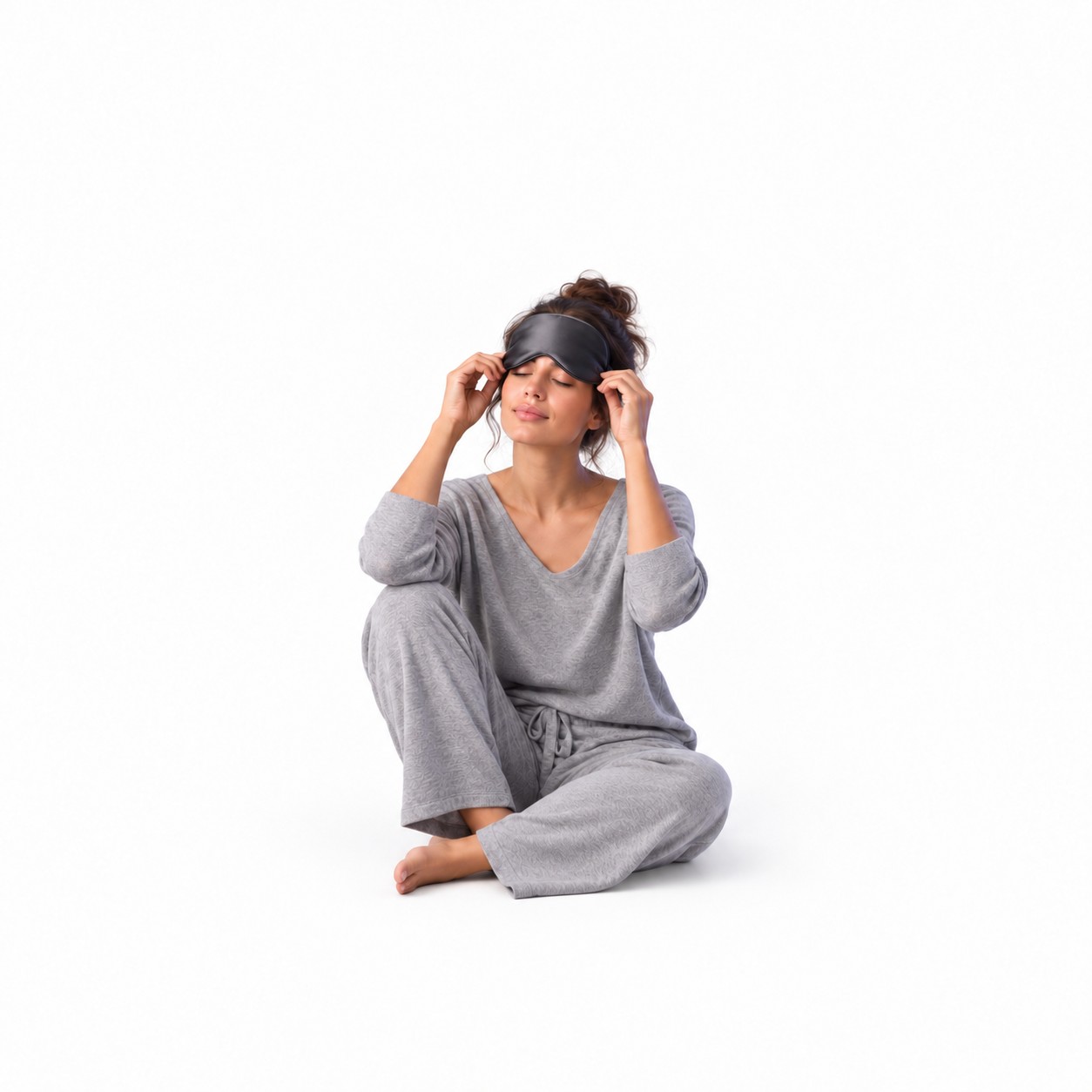 Woman in grey sleepwear adjusting a black sleep mask